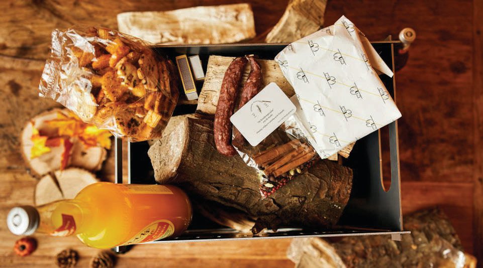 Kerstpakket in een stalen krat, gevuld met haardhout, ambachtelijke worst, koekjes en een fles sap