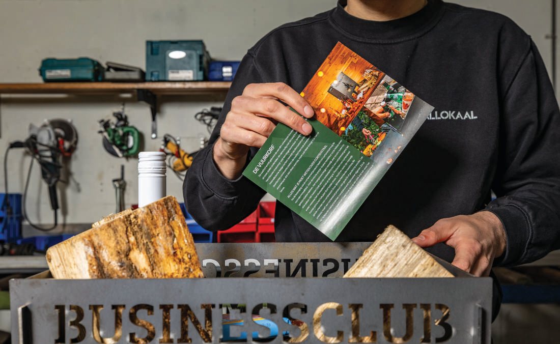 Medewerker legt een brochure in een stalen Businessclub-krat met haardhout en een fles