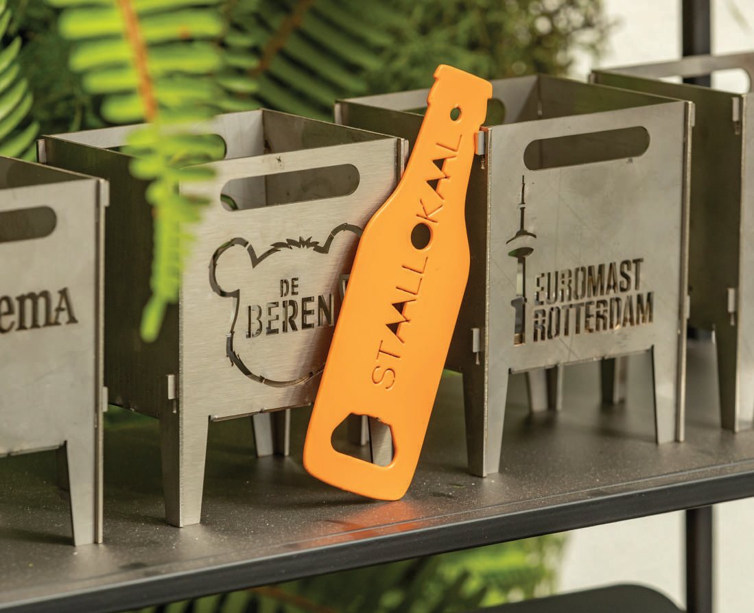 Stalen vuurkorven met uitgesneden bedrijfslogo's en een oranje flesopener van Staallokaal