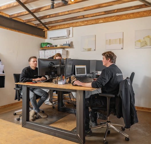 Twee teamleden werken samen aan een grote houten kantoortafel